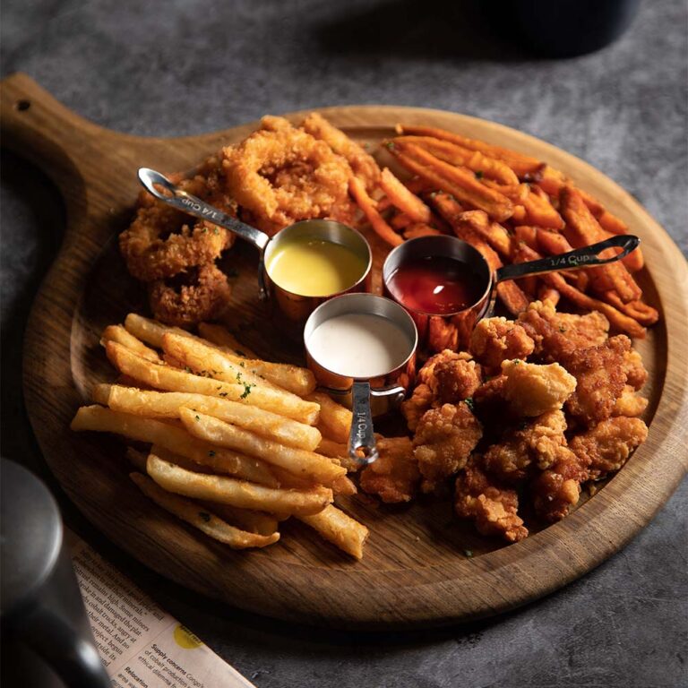 Round wooden serving platter with chips, fried crumbed calamari, battered chicken pieces surrounding dipping sauces in three tiny metal pots.